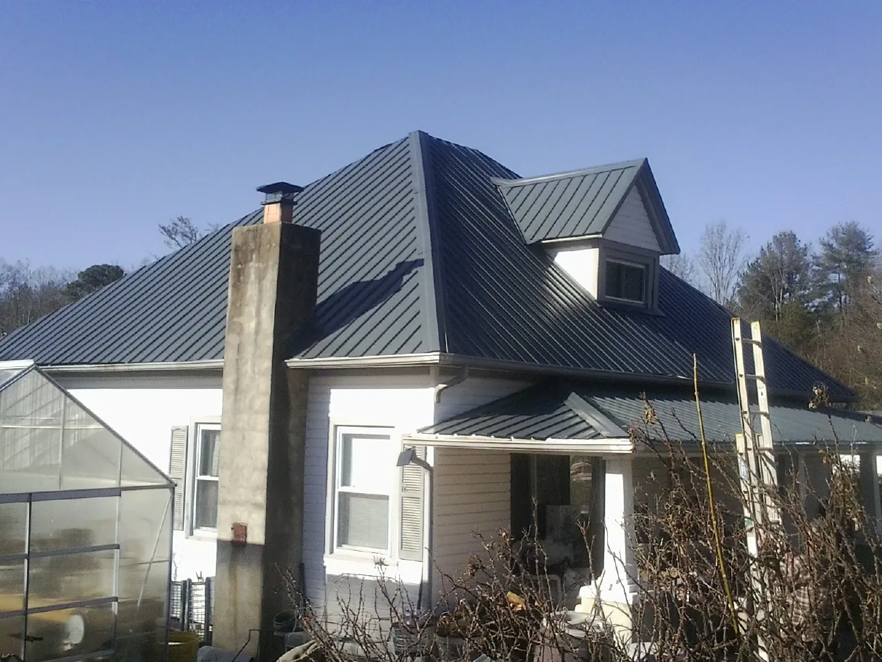 Dark blue standing seam metal roof on a white farmhouse with dormer — Slate & Tile Roof Repair by Roofing Brothers in Claxton