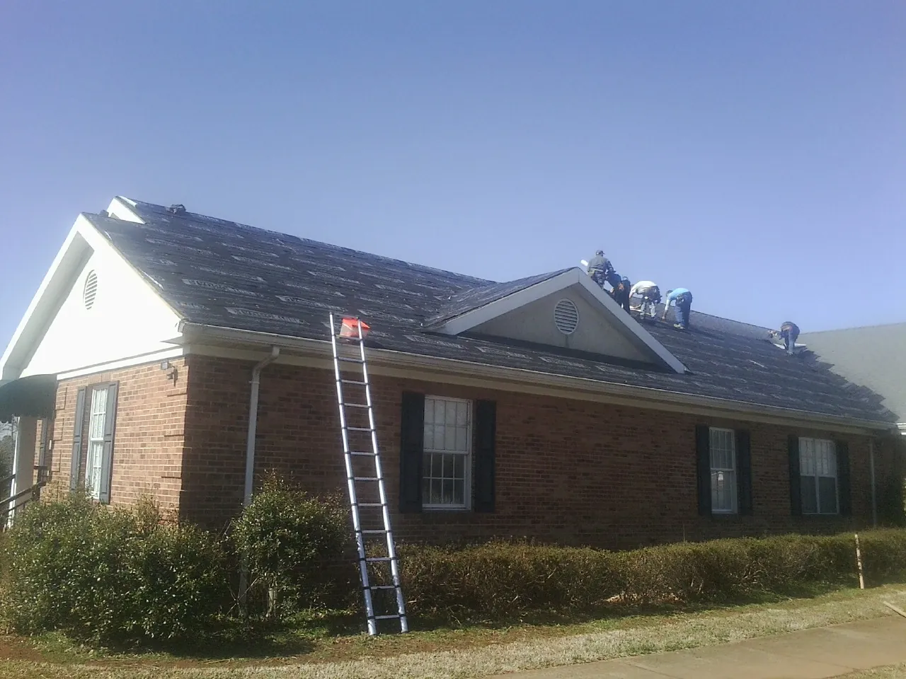 Crew tearing shingles off a brick ranch roof with a ladder set — Emergency Roof Repair work by our crew in Claxton