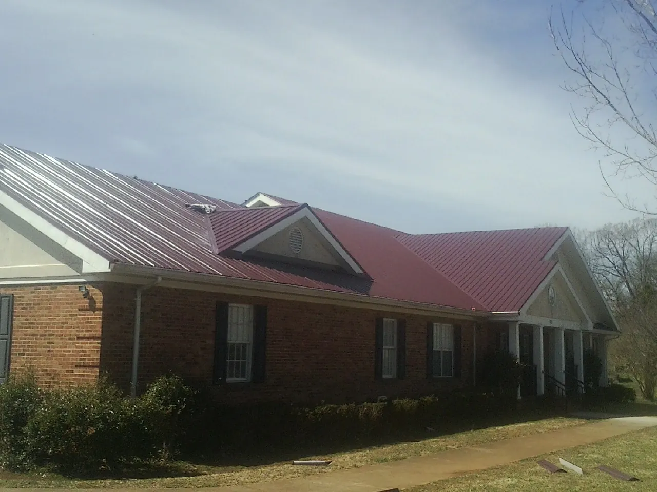 Red metal roof with gabled entries on a long brick building, from a Hail Damage Roof Repair job in Claxton