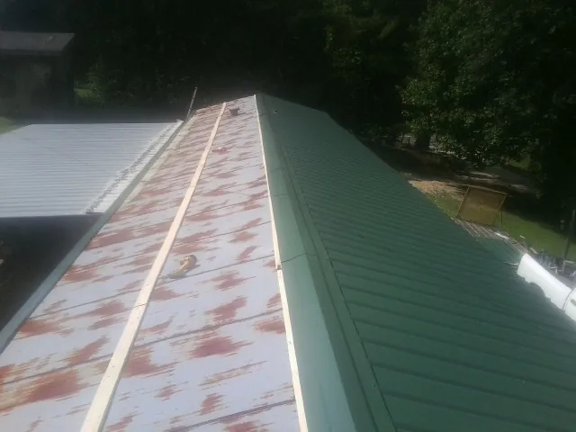 Old rusted panels beside newly installed green metal roofing — Wind Damage Roof Repair by Roofing Brothers in Claxton