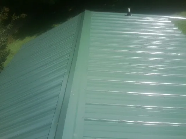 New green metal panels meeting at the ridge of a roof — Flat Roof Repair work by our crew in Claxton