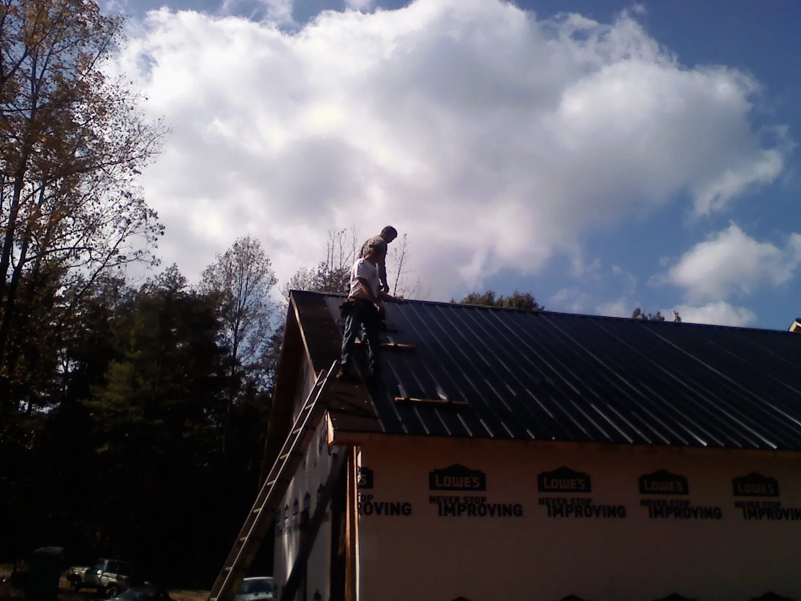 Roofer fastening dark metal panels high against a cloudy sky, from a Roof Inspection job in Claxton