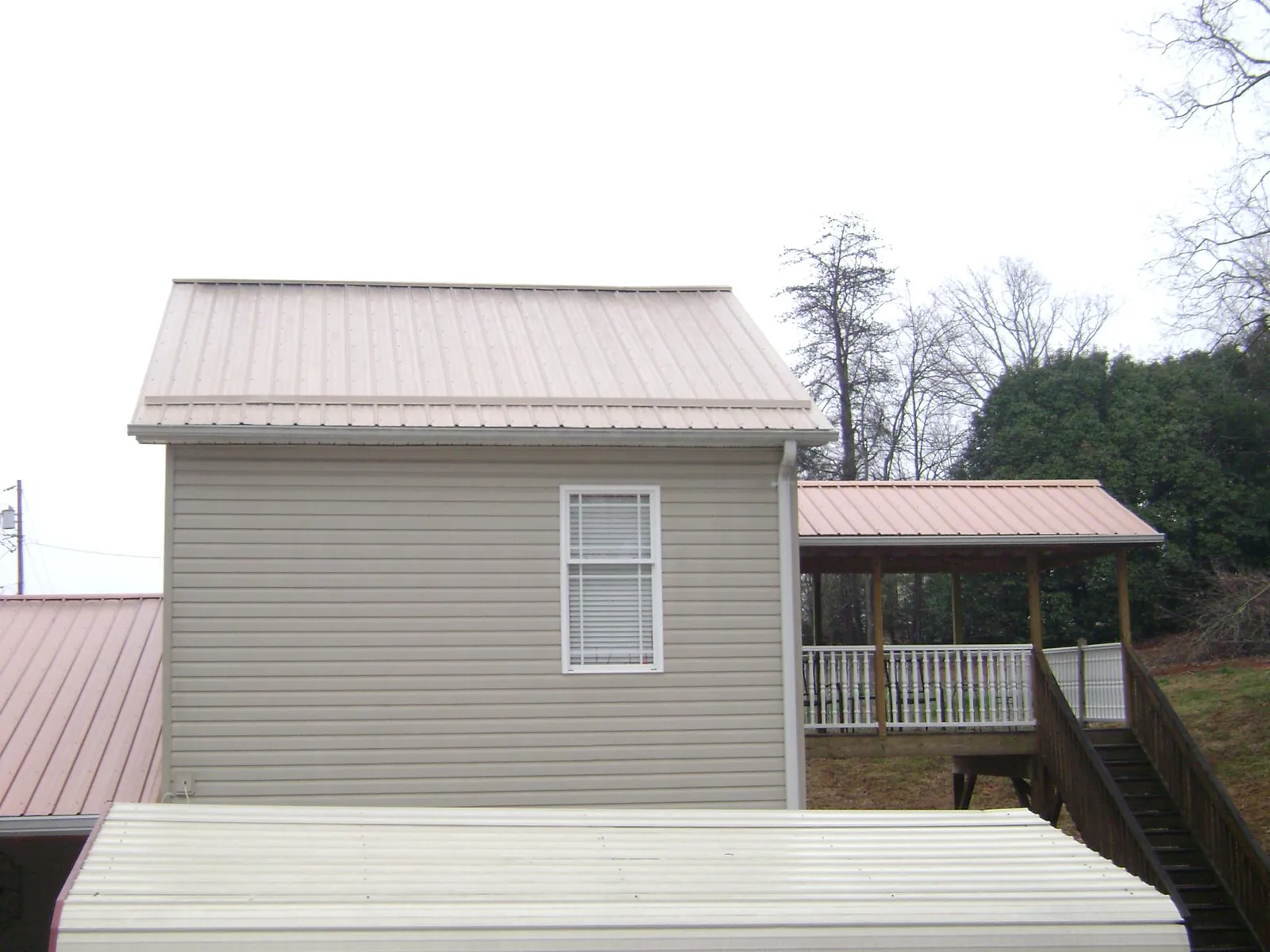Tan metal roofs on a two story addition and attached porch, from a Roof Replacement job in Claxton